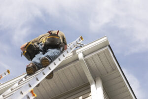 A handyman repairs his rain gutters. He is up a ladder, photo taken from ground looking up, low angle view. He wears a tool belt, sky and clouds, good copy space, roofers Peoria IL, roofing company Peoria IL, roof repair Peoria IL, roof replacement Peoria IL, residential roofing Peoria IL, commercial roofing Peoria IL, roofing contractor Peoria IL, roof inspection Peoria IL, storm damage roofing Peoria IL, hail damage roof repair Peoria IL, local roofers Peoria IL, emergency roof repair Peoria IL, roofing services Peoria IL, shingle roofing Peoria IL, flat roof repair Peoria IL, roof leak repair Peoria IL, Peoria roofing contractors, roofing estimates Peoria IL, Midwest roofing contractor, storm restoration Peoria IL