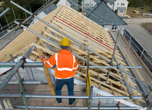 Aerial view of construction worker working on roof trusses, roofing company near me, top roofing company near me, best roofing company near me, local roofing company near me, roofing contractors near me, roof repair company near me, roof replacement company near me, residential roofing company near me, commercial roofing company near me, licensed roofing company near me, insured roofers near me, roof inspection company near me, storm damage roofing company near me, emergency roof repair near me, roofing estimates near me, shingle roofing contractor near me, flat roofing company near me, Central Illinois roofing company, trusted roofing contractor near me, nearby roofing services, professional roofers near me